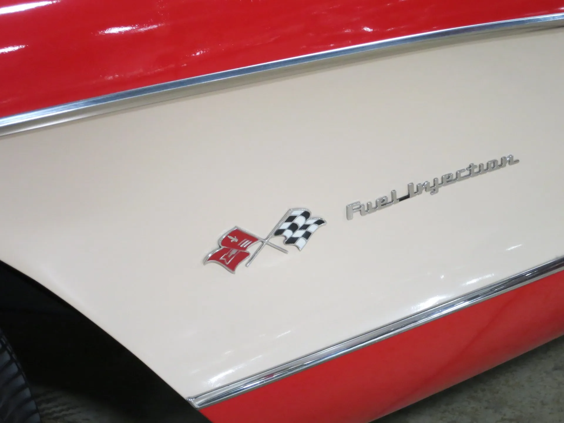A chrome crossed-flags emblem and Fuel Injection script on the white side cove of a red C1 Corvette.