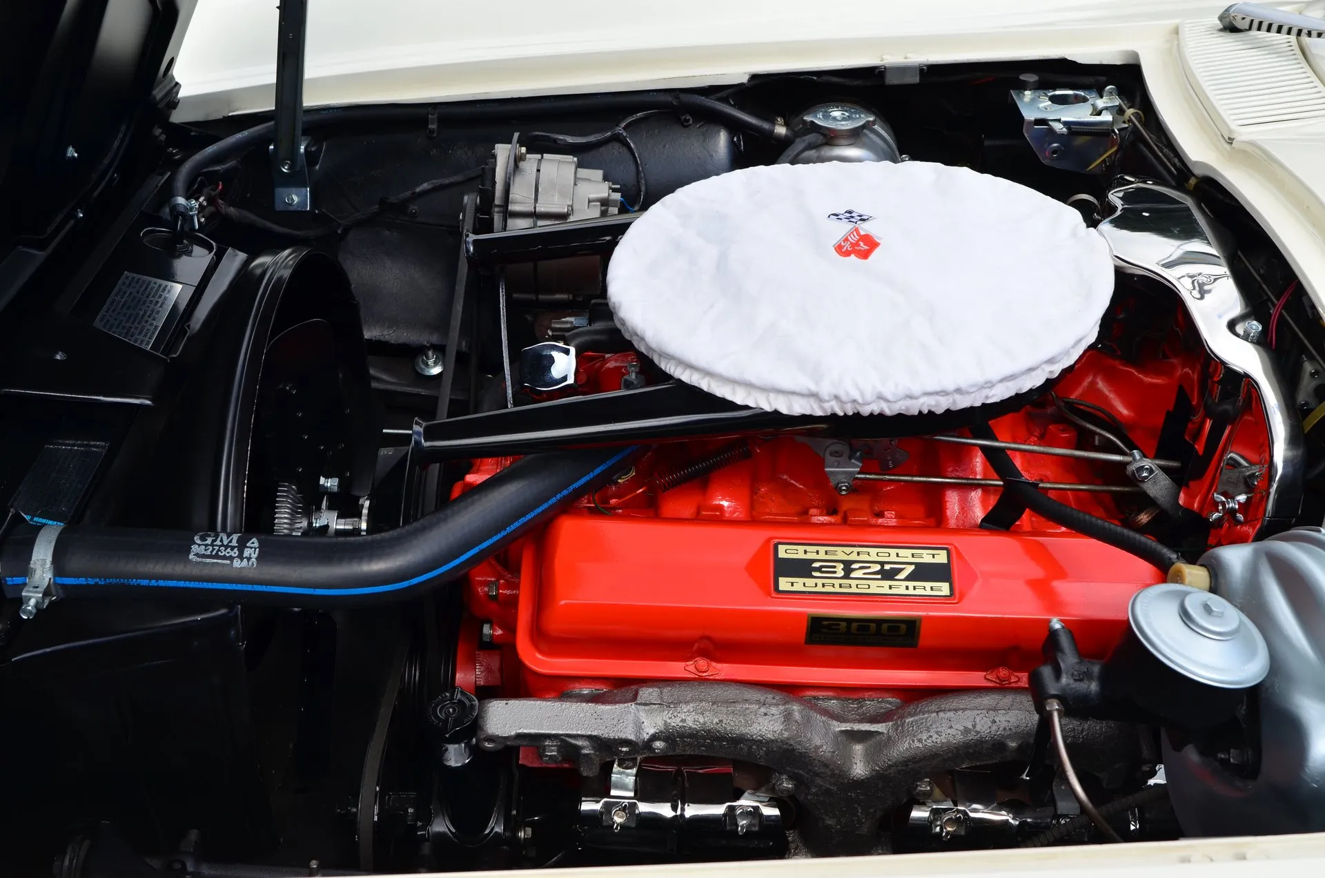 The engine bay of a 1963 Corvette coupe: an orange 327 V8 with a Chevrolet 327 Turbo-Fire decal and a 300 horsepower plate on the valve cover, a white cloth cover over the air cleaner, and the alternator and radiator cap behind it.