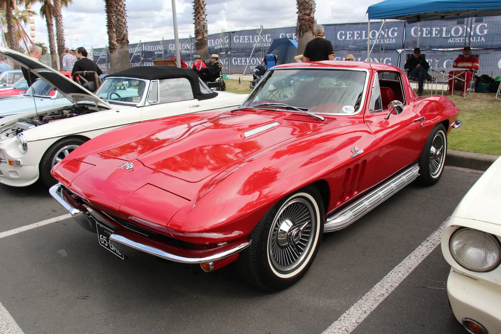 A red Corvette coupe at an outdoor car show in Geelong, Australia, seen from the front left, with a raised bulge down the middle of the hood, a 396 badge under the crossed-flags emblem on the front fender, three vertical fender vents and whitewall tires.