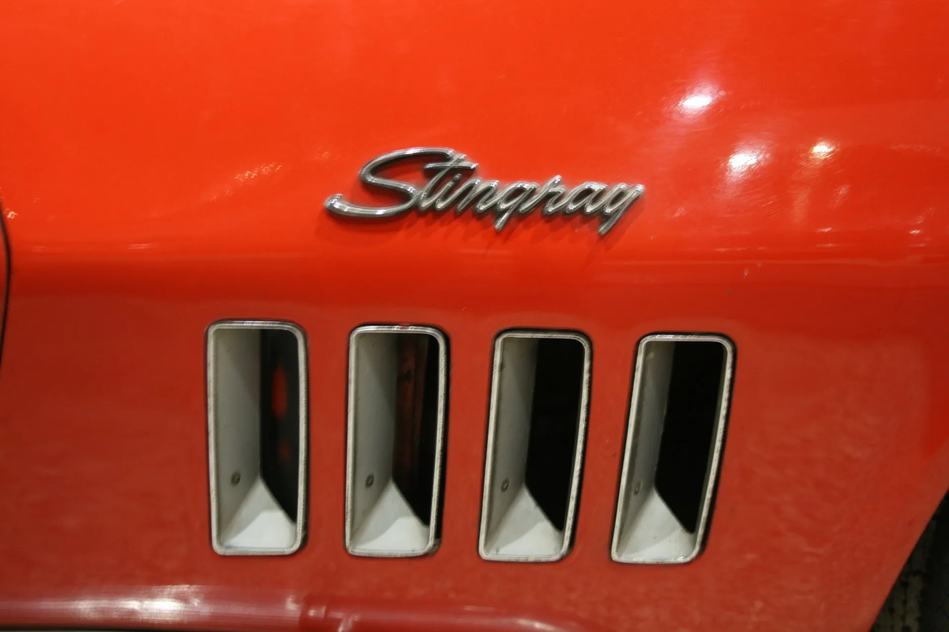 Close-up of chrome Stingray script above four vertical slot louvers on the red front fender of a 1969 Corvette.