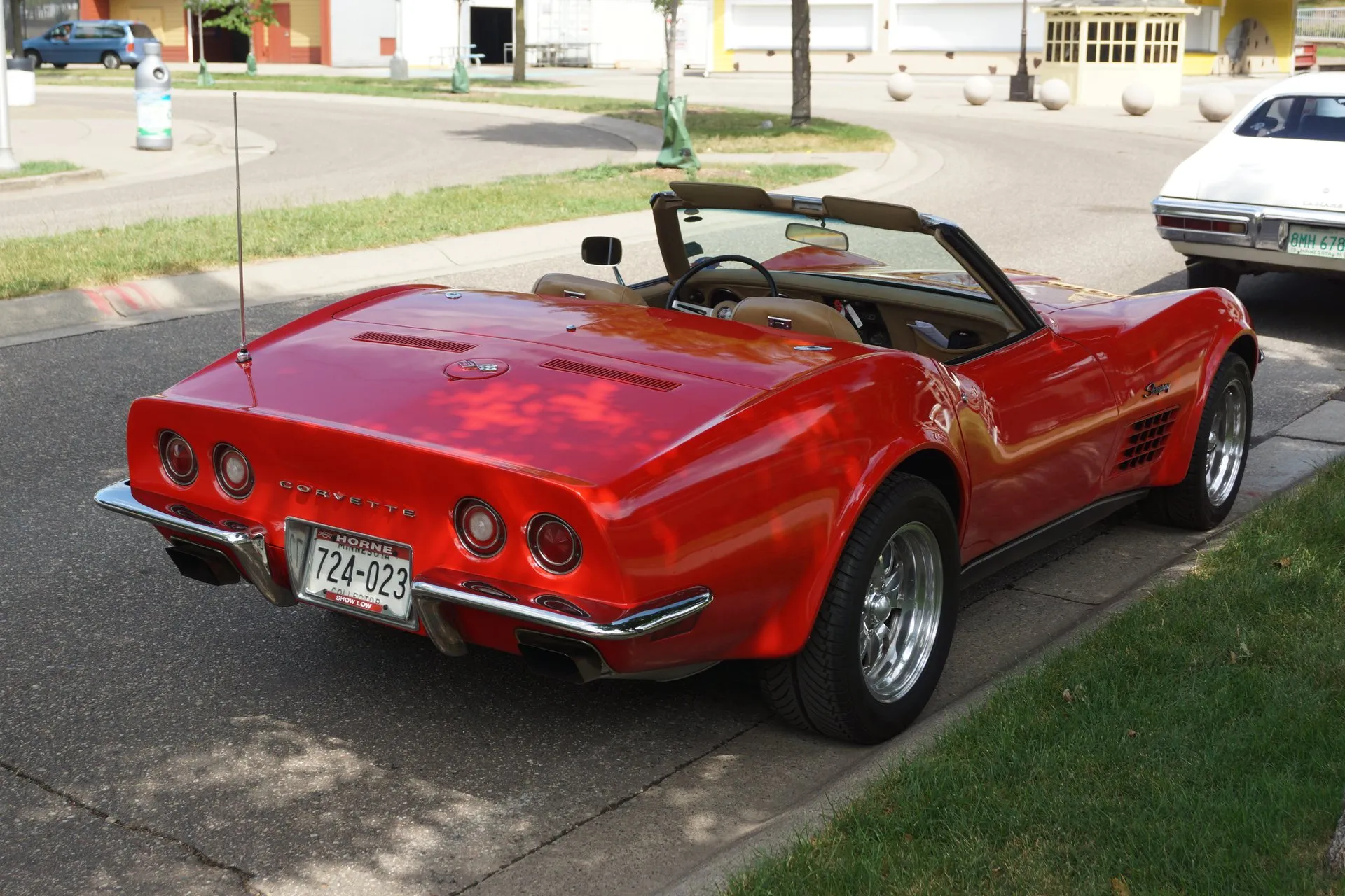 The same red convertible from the rear right with its top down, showing four round taillights, Corvette lettering across the tail, rectangular exhaust outlets under the chrome bumper and a Minnesota plate in a dealer frame.