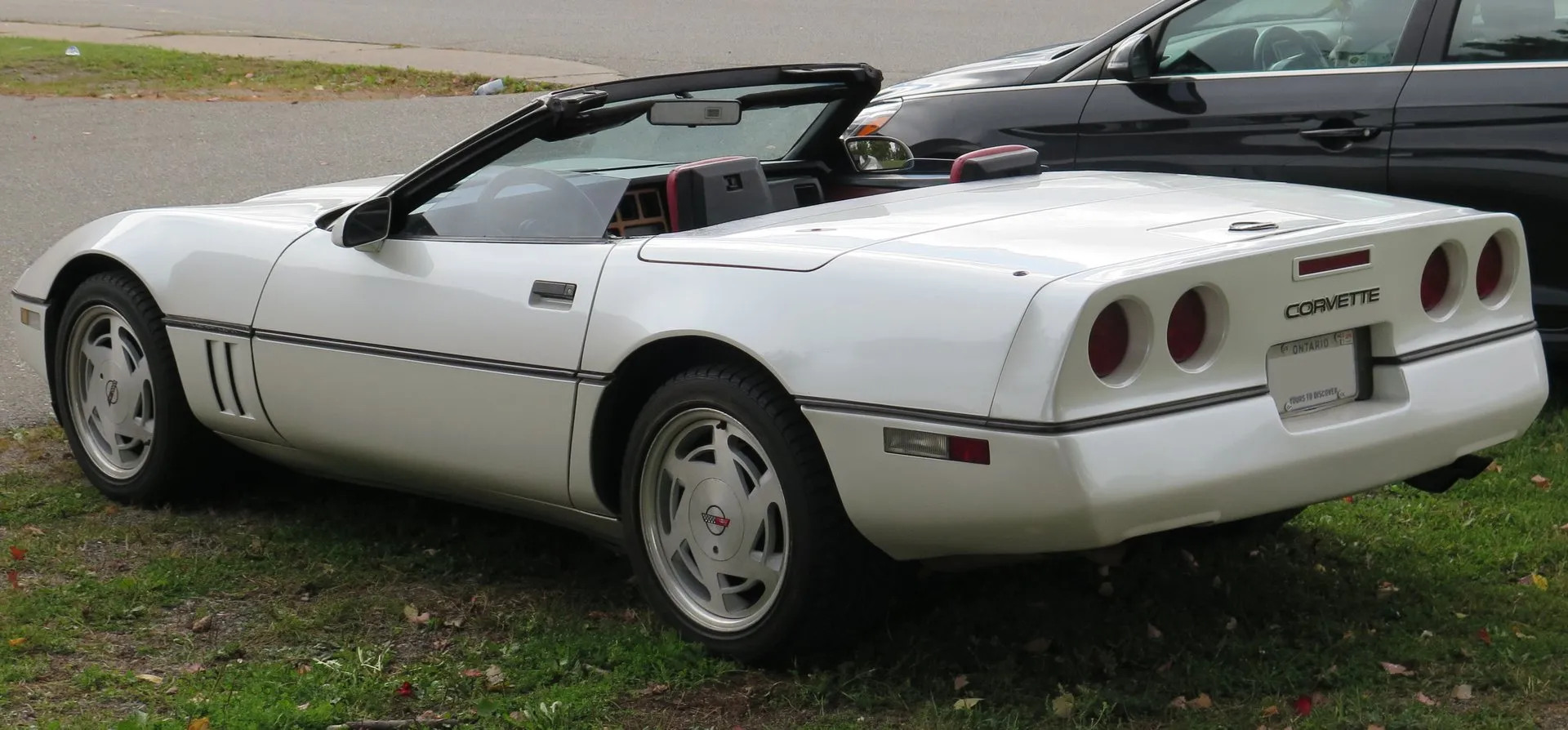 The same white 1988 Corvette convertible seen from the rear left, top down, with four round taillights, a red interior and the six-vent wheels.