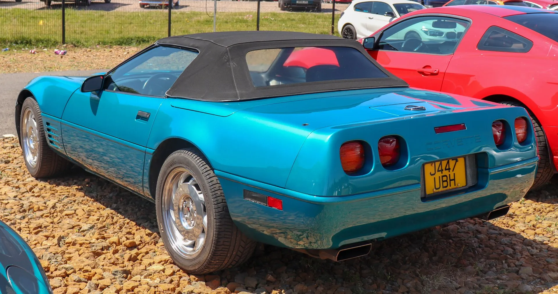 The same Bright Aqua Metallic C4 convertible seen from the rear left, showing its four taillamps, the convex rear fascia and two rectangular exhaust outlets under the bumper.
