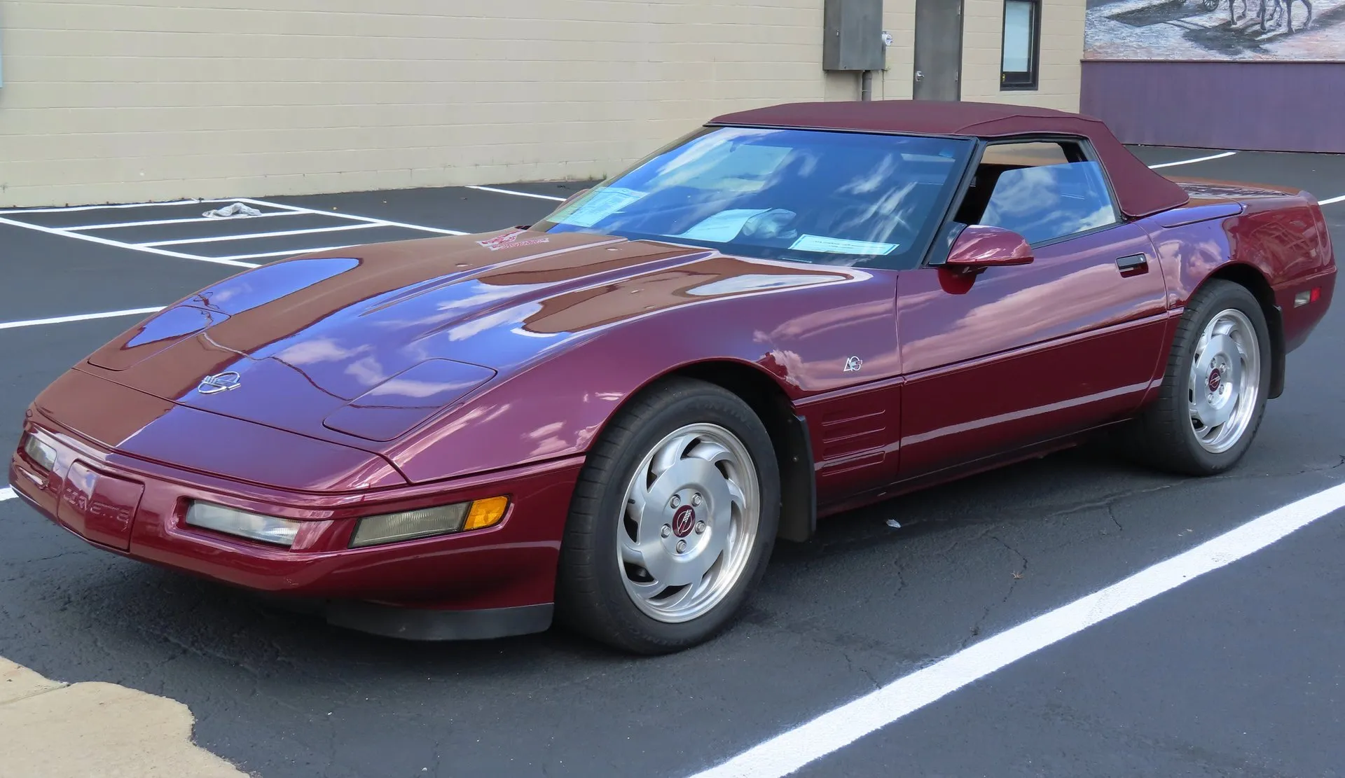 Ruby Red C4 Corvette convertible with a matching dark red soft top raised, parked in an empty lot, seen from the front left, with silver wheels and red center inserts.
