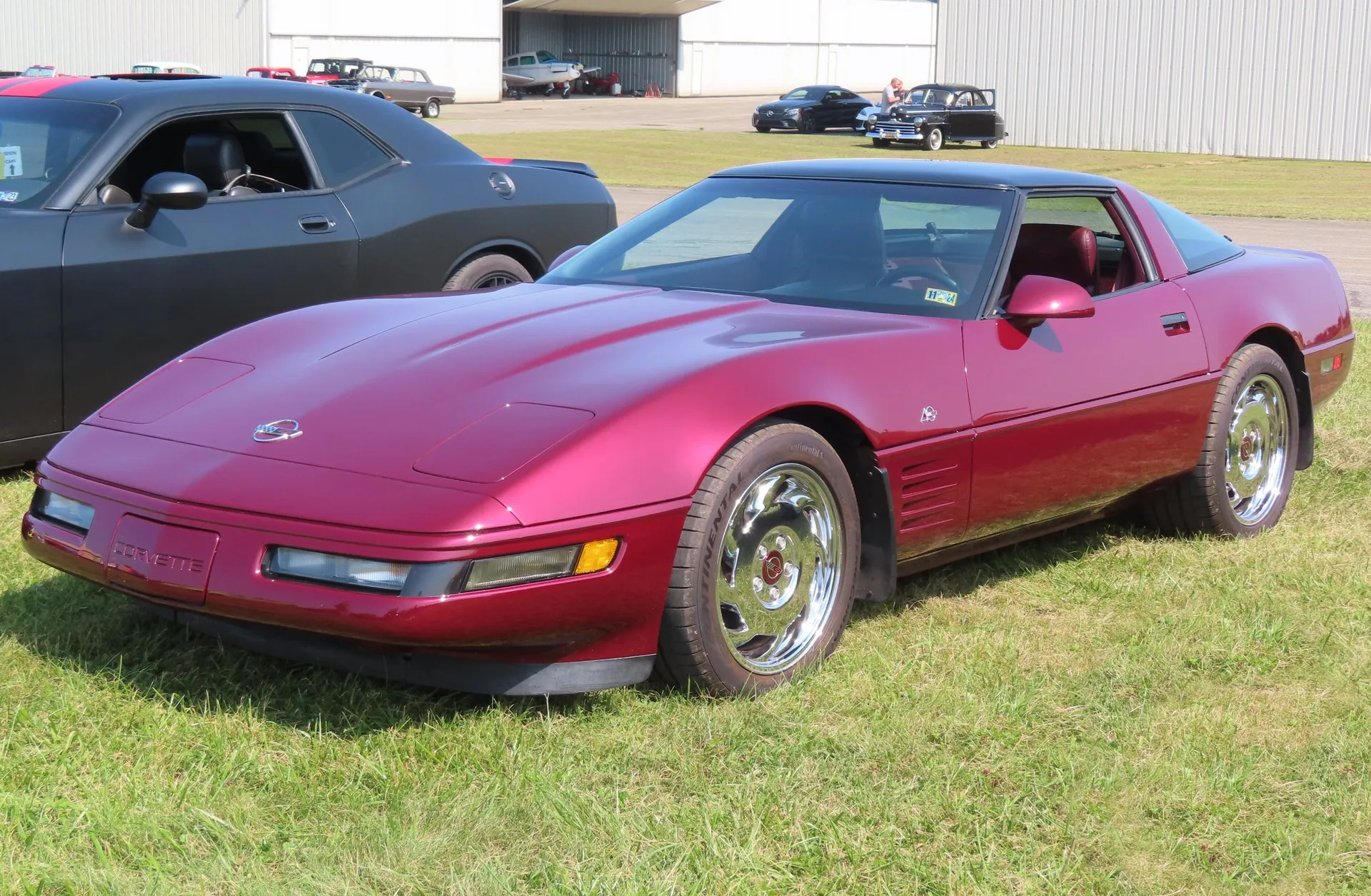 Ruby Red C4 Corvette coupe with a black roof, a red interior and chrome-finish wheels, parked on grass at an airfield car show, seen from the front left.