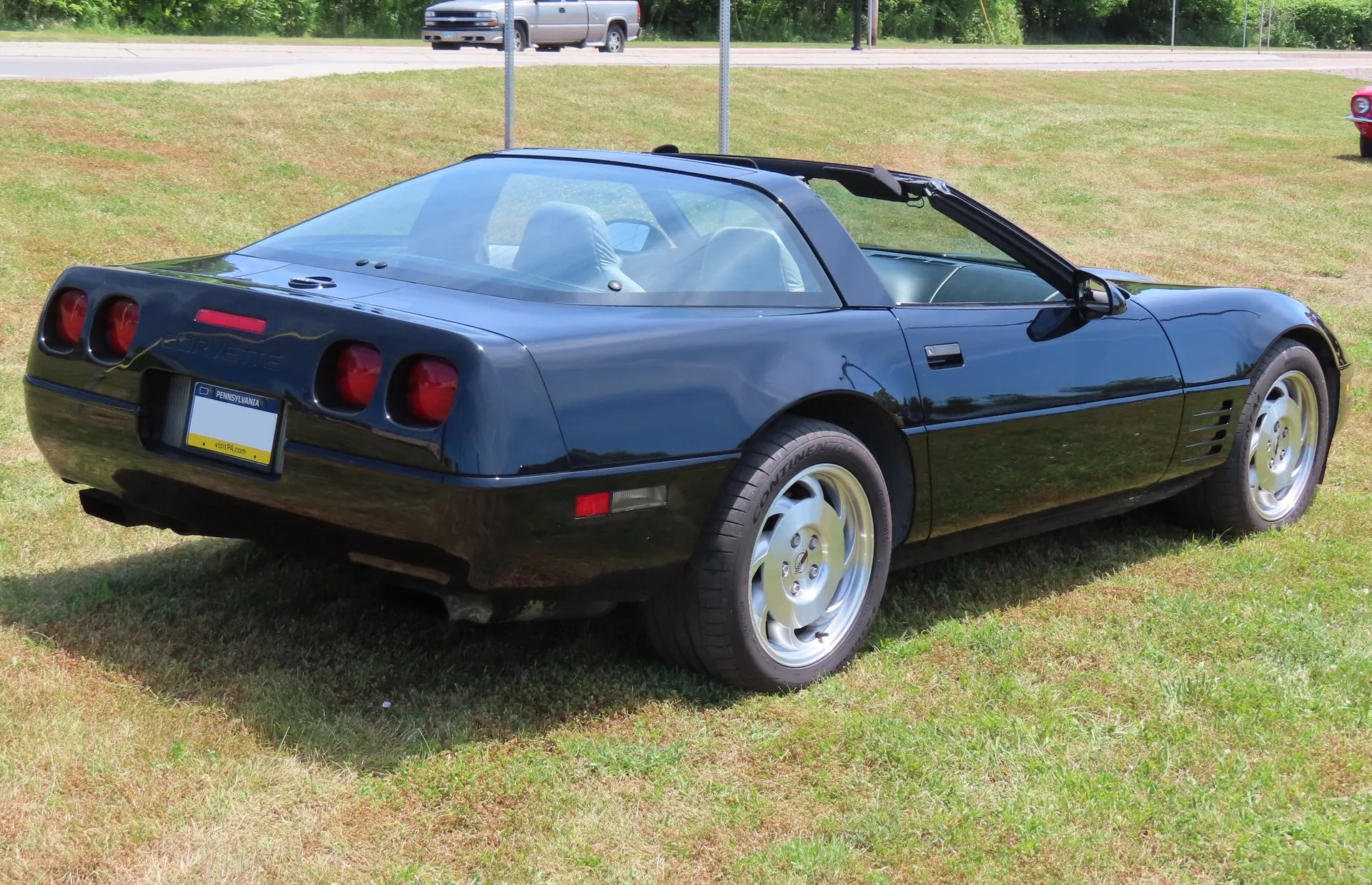 The black C4 Corvette coupe from the rear right with its roof panel off, showing four round red taillamps, Corvette lettering on the rear fascia and a Pennsylvania plate frame.