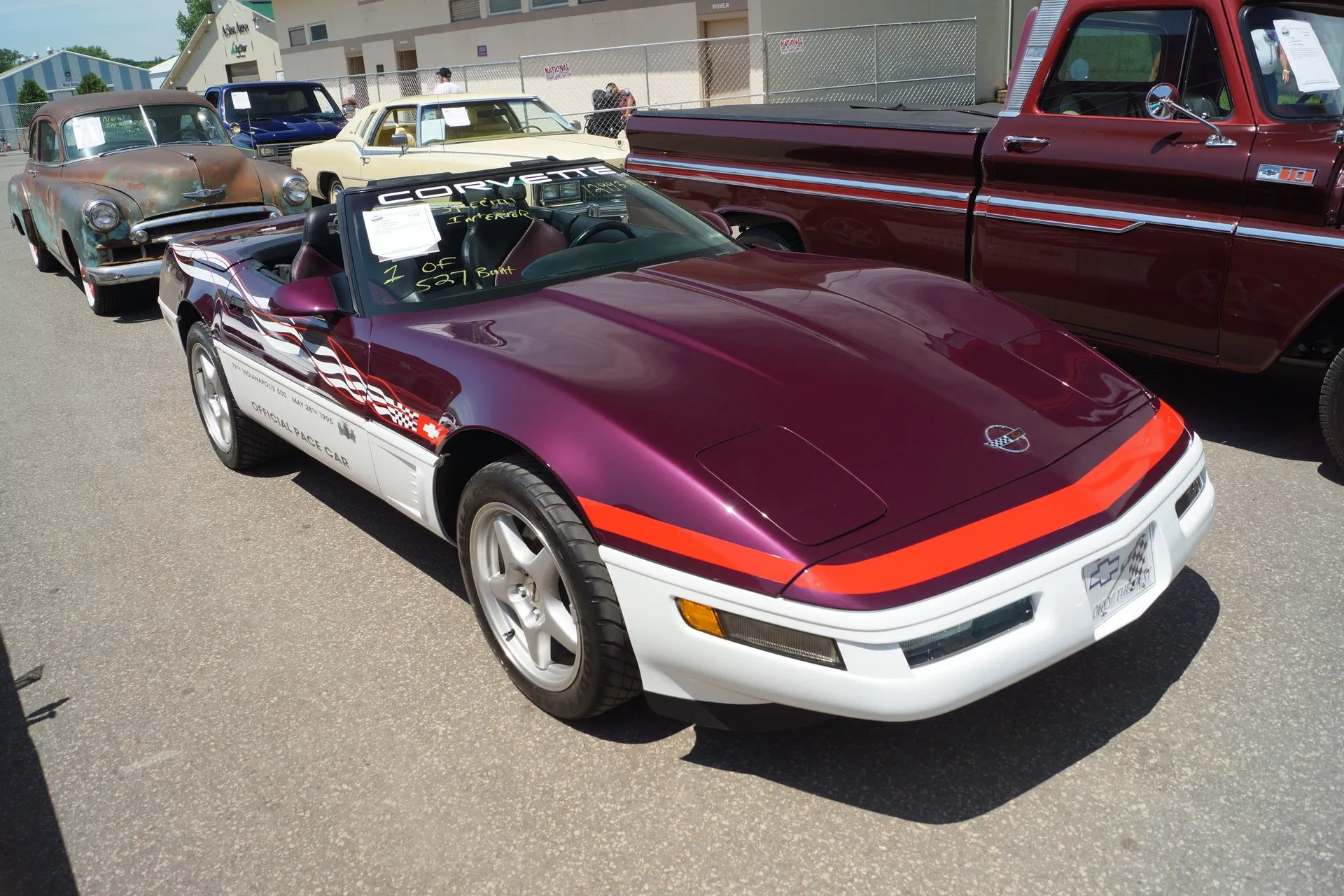 Dark purple and white C4 Corvette convertible with its top down at an outdoor car show, seen from the front left, with a red stripe across the nose, Official Pace Car lettering on the door and 1 of 527 written on the windshield.