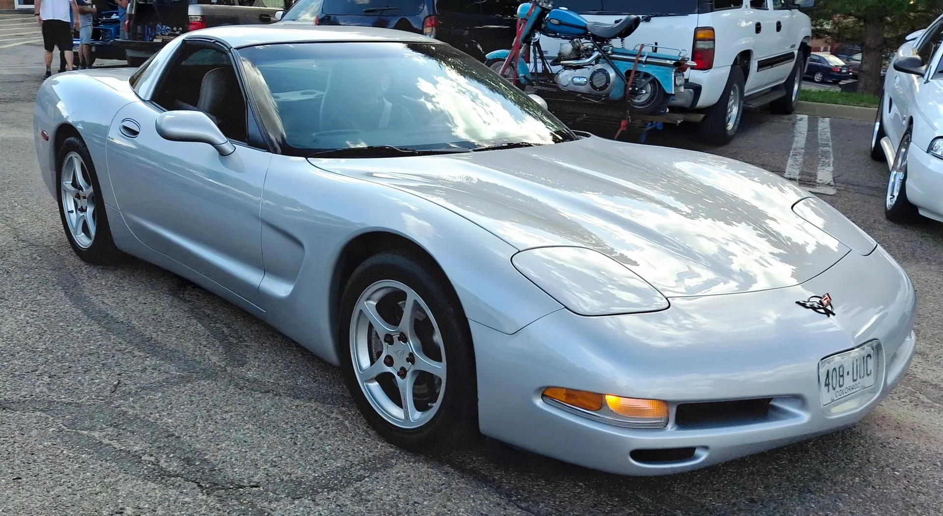 Silver C5 Corvette coupe in a parking lot at a car cruise, seen from the front right, with thin five-spoke silver wheels, pop-up headlights closed and a Colorado license plate.