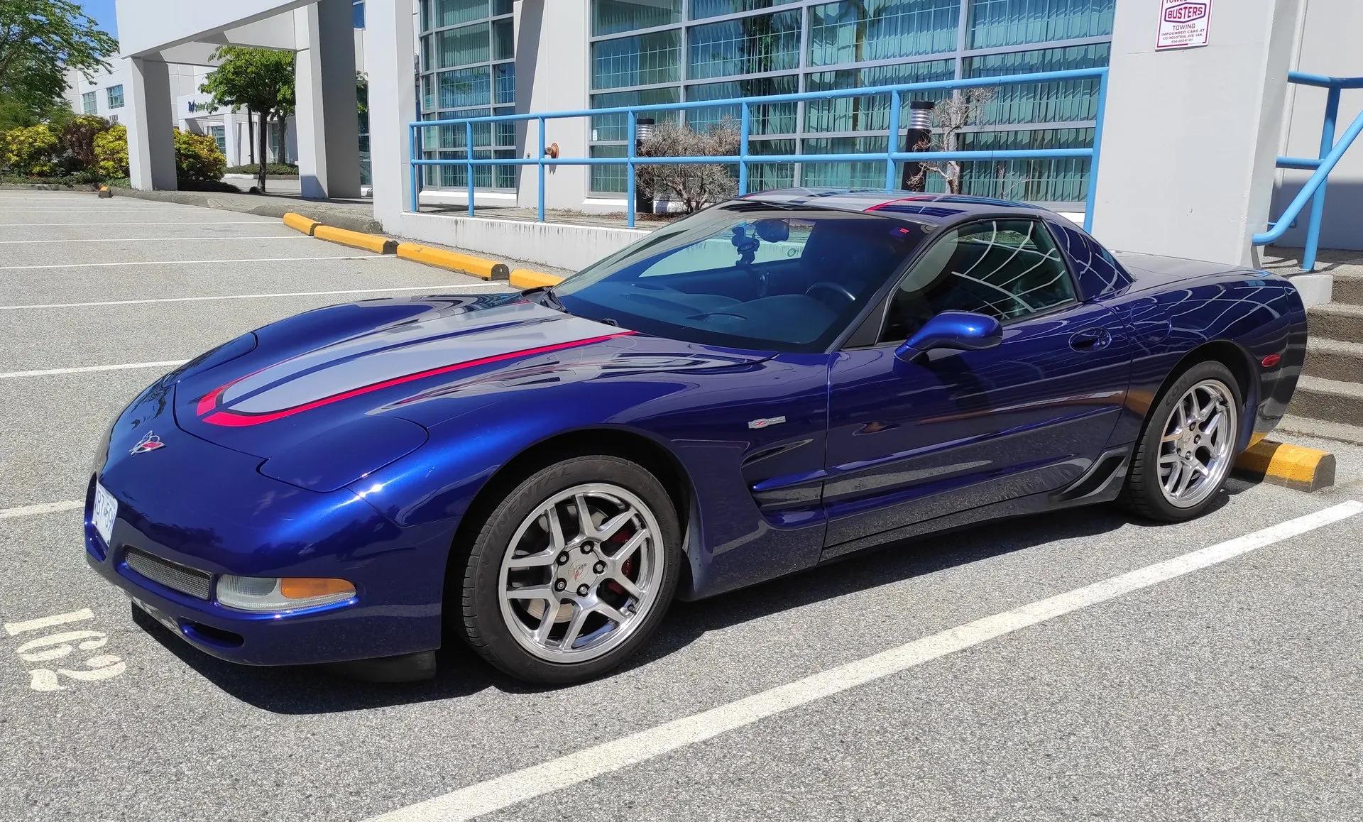 Le Mans Blue 2004 Corvette Z06 Commemorative Edition in a parking lot, seen from the front left, with a wide silver stripe edged in red over the hood and roof, a Z06 badge on the front fender and polished Z06 wheels.