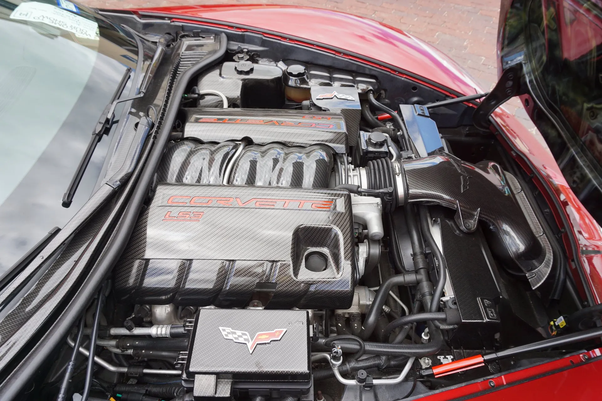 Engine bay of a red C6 Corvette seen from above, with carbon-look covers over the LS3 engine, the fuse box and the air intake.