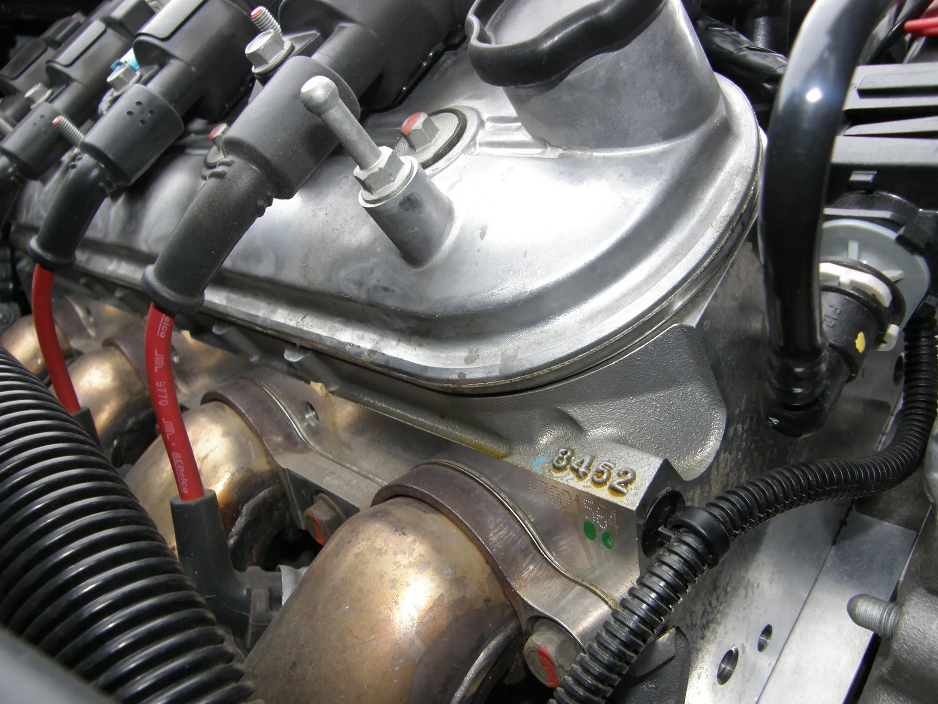 Close-up of the side of a C6 Corvette Z06's LS7 engine: the aluminum valve cover and cylinder head with a cast 8452 number, coil packs, red spark plug wires and the exhaust header flanges.